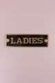 Gold and black metal 'Ladies' door sign on a light pink wall, G Decor home hardware