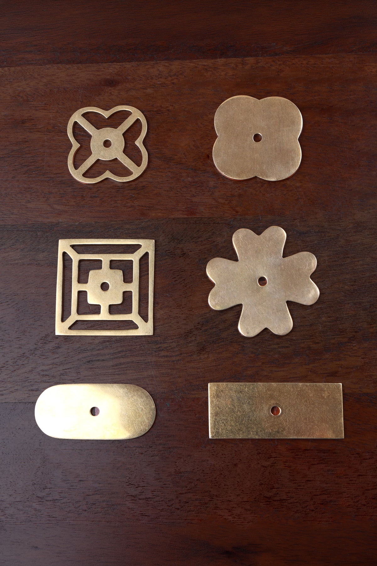 Six aged brass backplates — pierced and solid quatrefoil, square fretwork, flower, oblong and rectangle