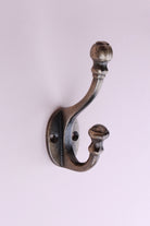 Ball Finial Hook: cast iron double hook with a ball top on a turned collar and a flared lower tip, on an oval back plate, antique brass finish