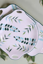 The round leaf plate resting on the long leaf platter, both white ceramic with green rims