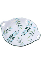 Round white ceramic serving plate with green and blue leaves and two cut-out handles, on white