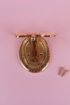 Brass butterfly door knocker lifted to show the oval back plate with its decorated rim and two screw holes