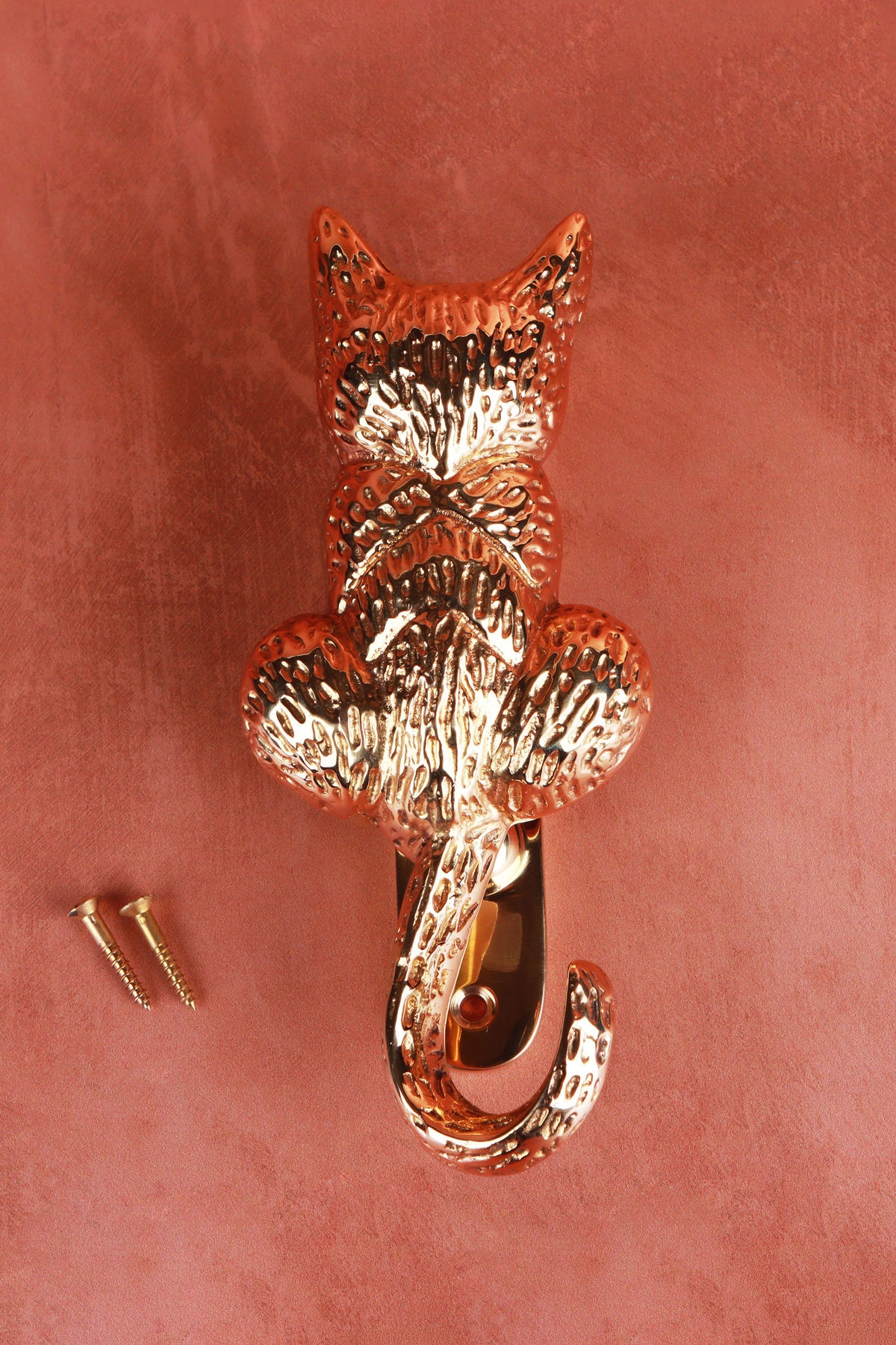 Brass cat door knocker on a terracotta background with its two fixing screws