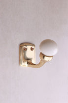 Cream ceramic ball hook: a cream ceramic ball on a curved brass-finish hook with a small back plate and two screws