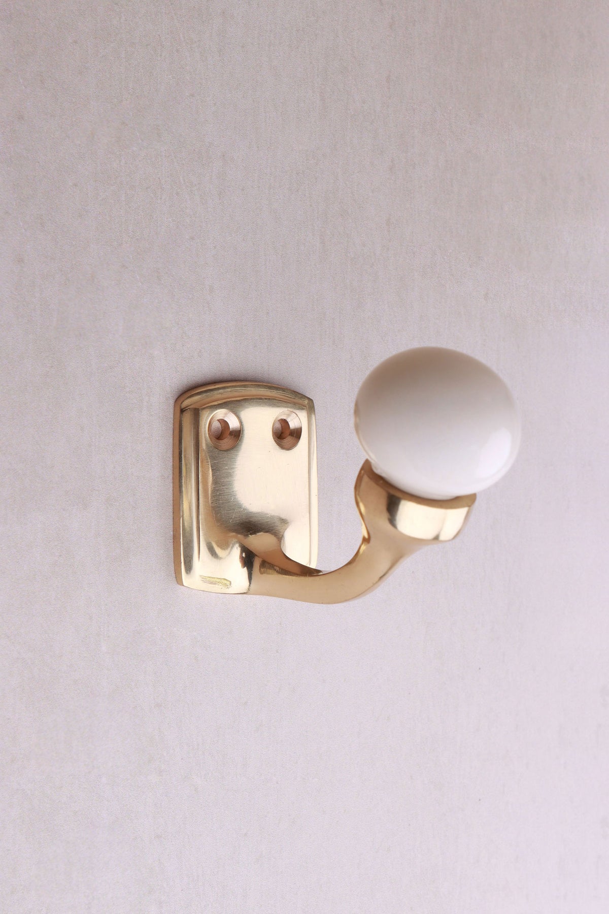 Cream ceramic ball hook: a cream ceramic ball on a curved brass-finish hook with a small back plate and two screws