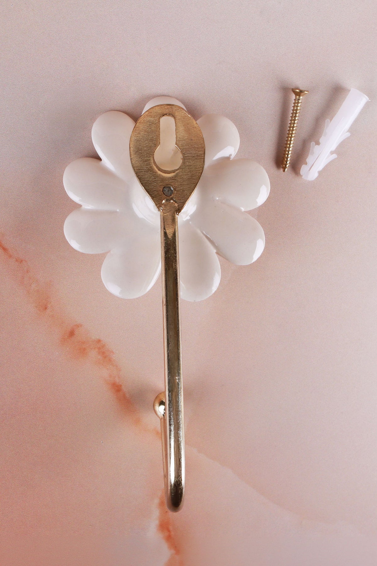 Back of the ceramic daisy wall hook showing the keyhole slot on the gold-tone plate, with the screw and wall plug