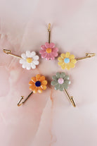 Five ceramic daisy wall hooks laid out on pink marble, showing the gold-tone metal hooks