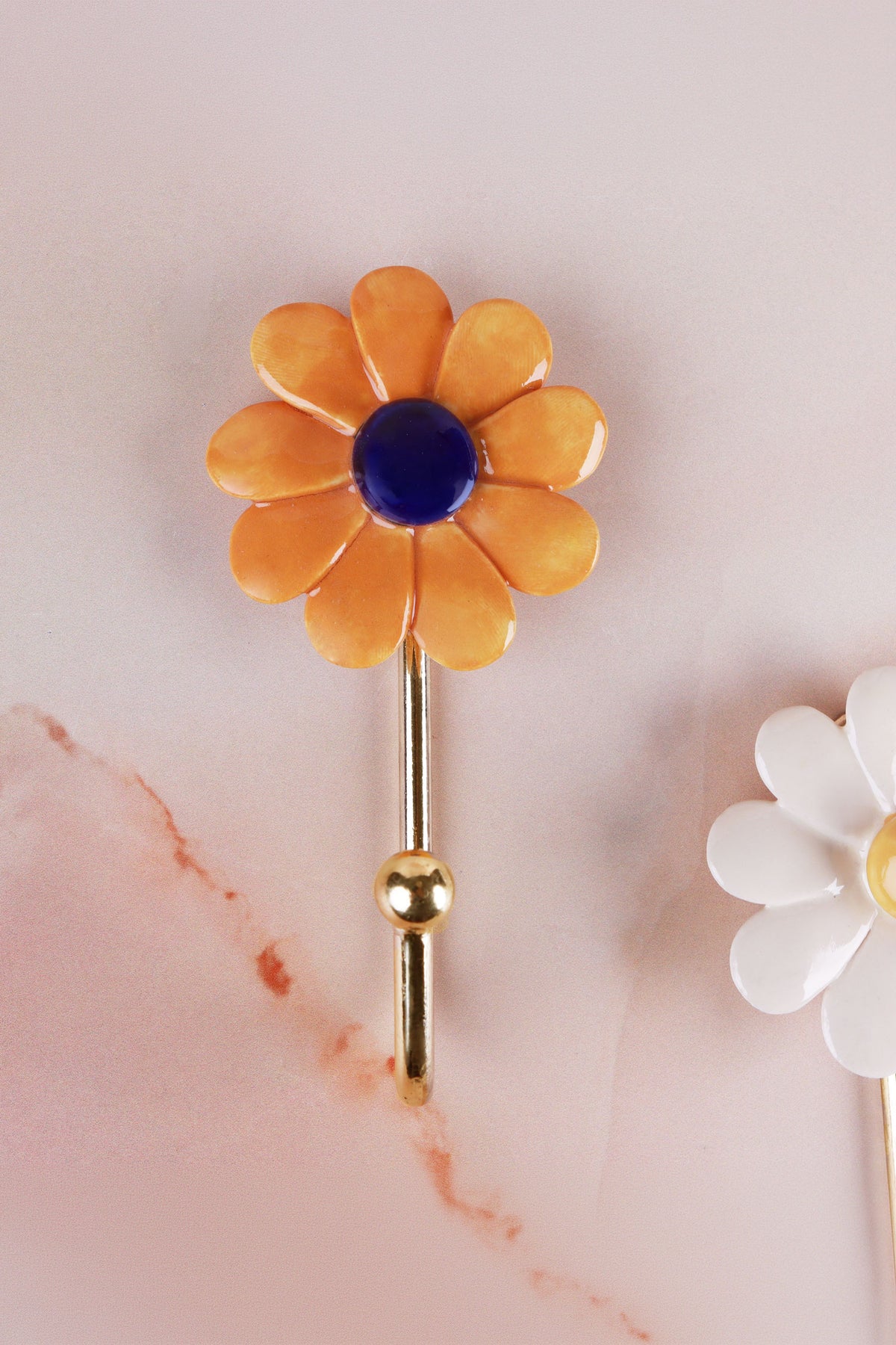 Dark yellow ceramic daisy wall hook with deep marigold petals and a navy blue centre on a gold-tone metal hook