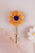 Dark yellow ceramic daisy wall hook with deep marigold petals and a navy blue centre on a gold-tone metal hook