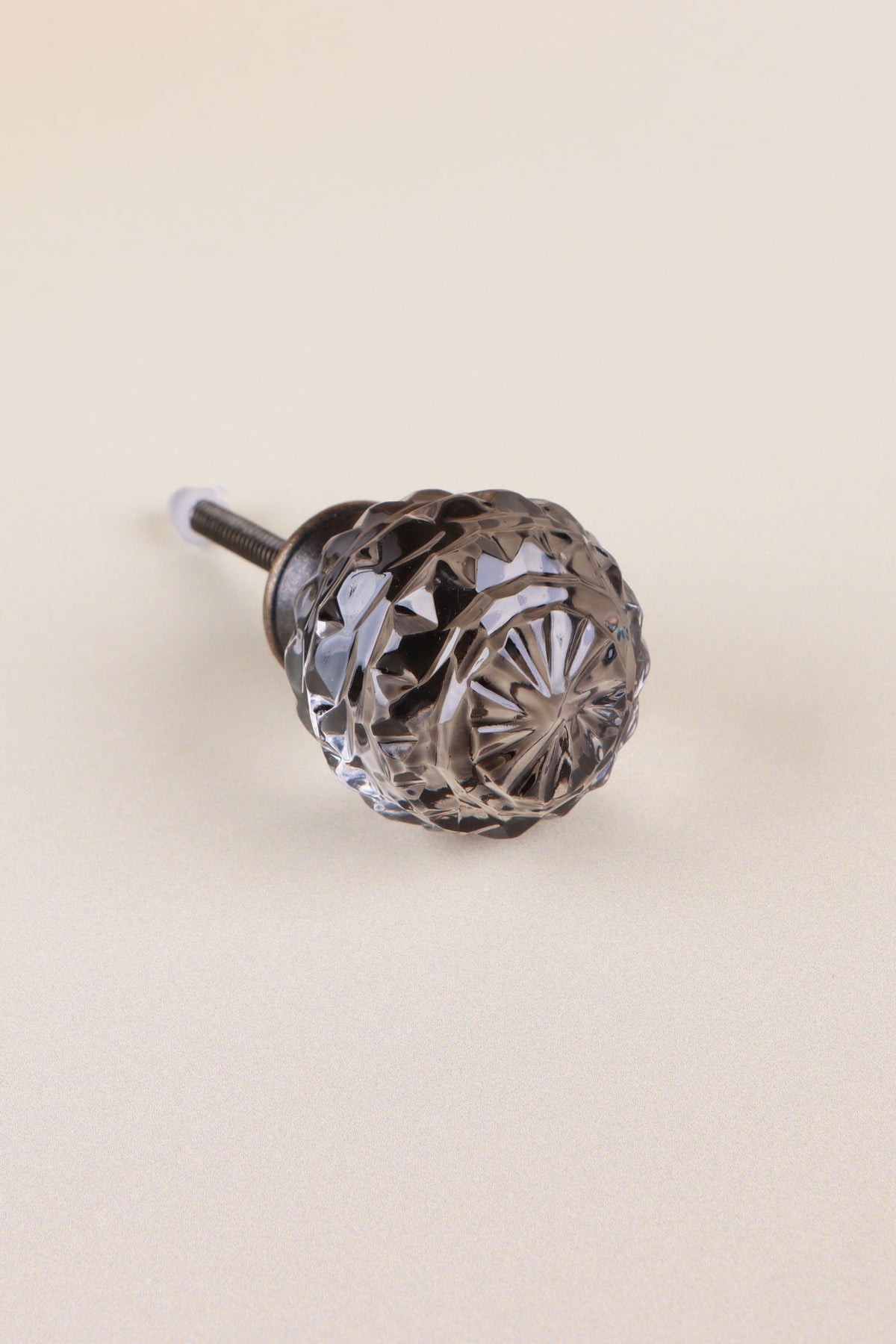 Smokey Grey faceted glass ball cabinet knob with a star cut on the front, on an antique brass finish base with its fixing bolt