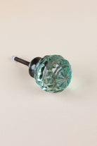 Teal faceted glass ball cabinet knob, a cool blue-green, on an antique brass finish base with its fixing bolt