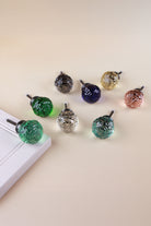 Eight faceted glass ball cabinet knobs on antique brass finish bases: emerald and light green, smokey grey, navy blue, ivory, blush pink, clear and teal, by the corner of a white cupboard door