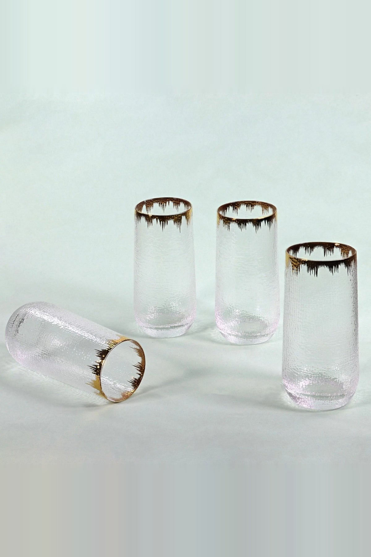 Three hammered glass tumblers standing and one lying on its side, showing the gold splash rim