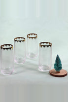Four tall hammered glass tumblers with gold splash rims on a pale background next to a small Christmas tree on a wood slice