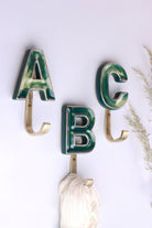 Green ceramic letter wall hooks with gold rims on gold-tone hooks