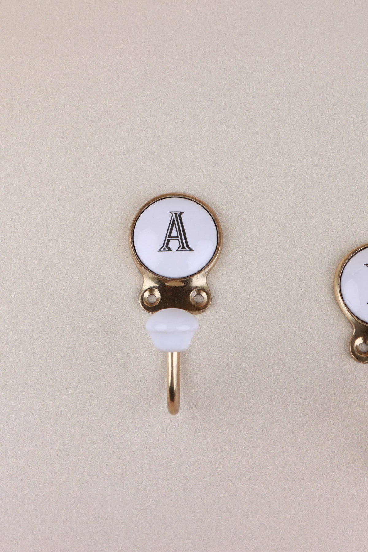 Letter A ceramic hook: white disc with a black serif capital A in a gold-tone frame, with a white ceramic knob