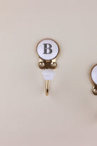 Letter B ceramic hook: white disc with a black serif capital B in a gold-tone frame, with a white ceramic knob