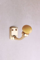 Mustard yellow ceramic ball hook: a mustard yellow ceramic ball on a curved brass-finish hook with a small back plate and two screws