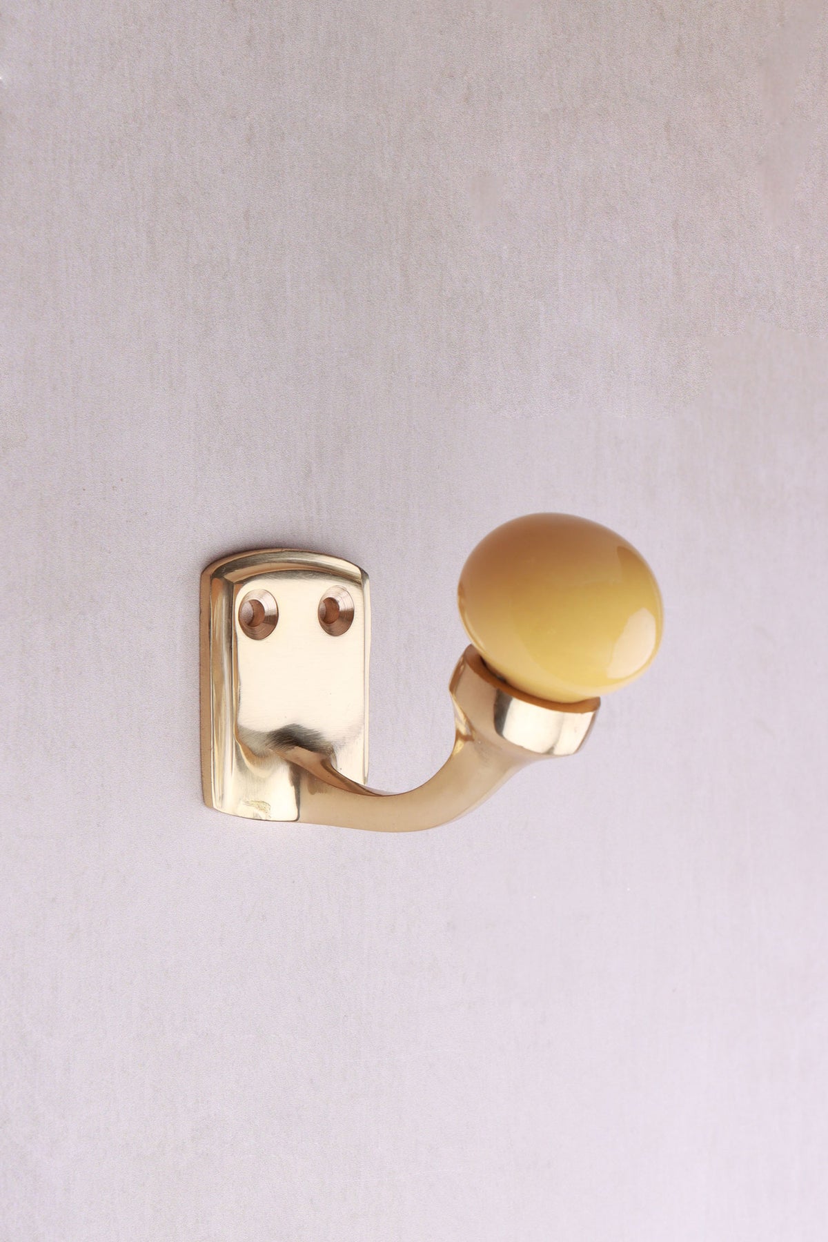 Mustard yellow ceramic ball hook: a mustard yellow ceramic ball on a curved brass-finish hook with a small back plate and two screws