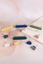 Six oval ceramic knobs and six long ceramic handles laid out on pink marble and a wooden board