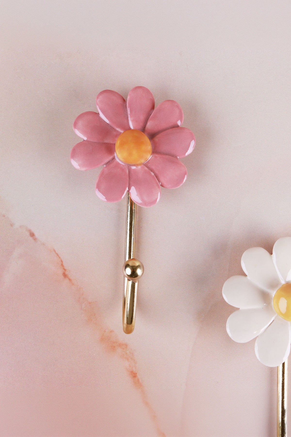 Pink ceramic daisy wall hook with a yellow centre on a gold-tone metal hook