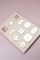 Eleven polished brass cabinet knob backplates on a pale wooden board: round, oval, square, squircle, quatrefoil, pierced, fretwork, flower, star, oblong and rectangle
