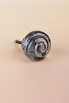Smokey Grey small rose glass cabinet knob with a swirl curling into the centre, on an antique brass finish base