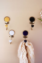 Ceramic coat hooks in yellow, black, white and dark blue, each with a matching ceramic knob, a lace cloth hanging from the dark blue hook