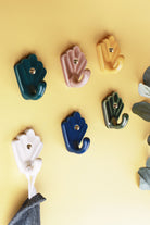 Scallop shell ceramic hooks in six glazes on a yellow wall, a striped cloth hanging from the cream hook