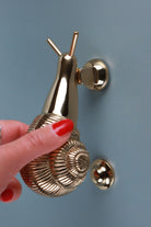 Hand lifting the brass snail door knocker by its shell above the strike button