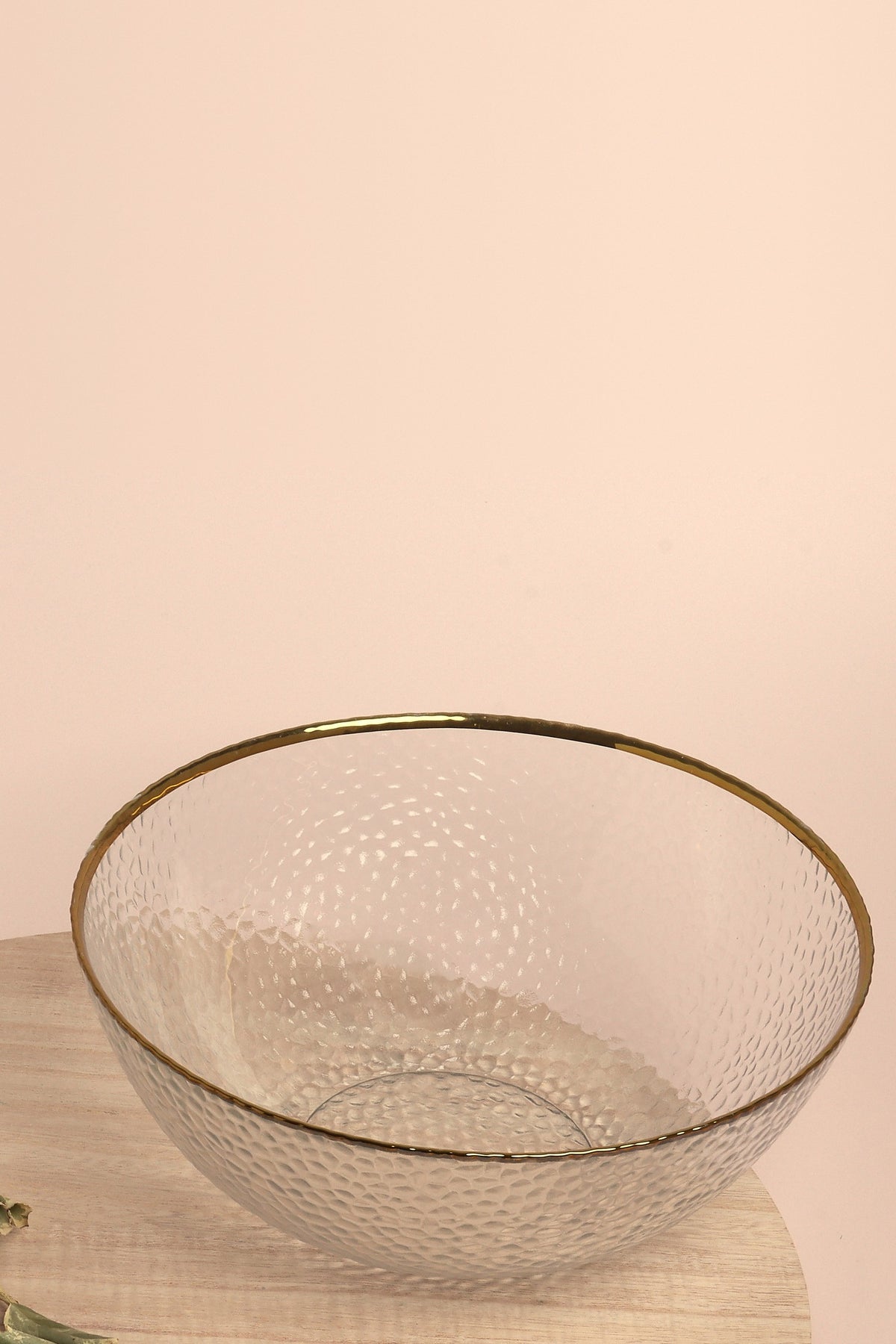 Thalia large clear glass bowl with a hammered texture and gold rim on a round wooden board