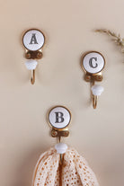 Three ceramic letter wall hooks, A, C and B, with a crochet lace cloth hanging from the B hook