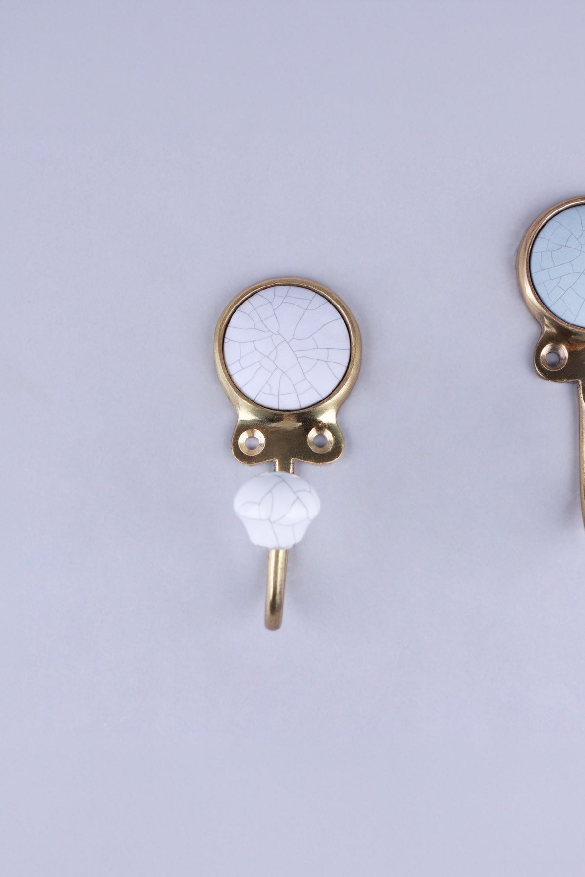 White crackle glaze ceramic coat hook: white disc with fine grey crackle lines in a gold-tone frame, with a white crackle knob