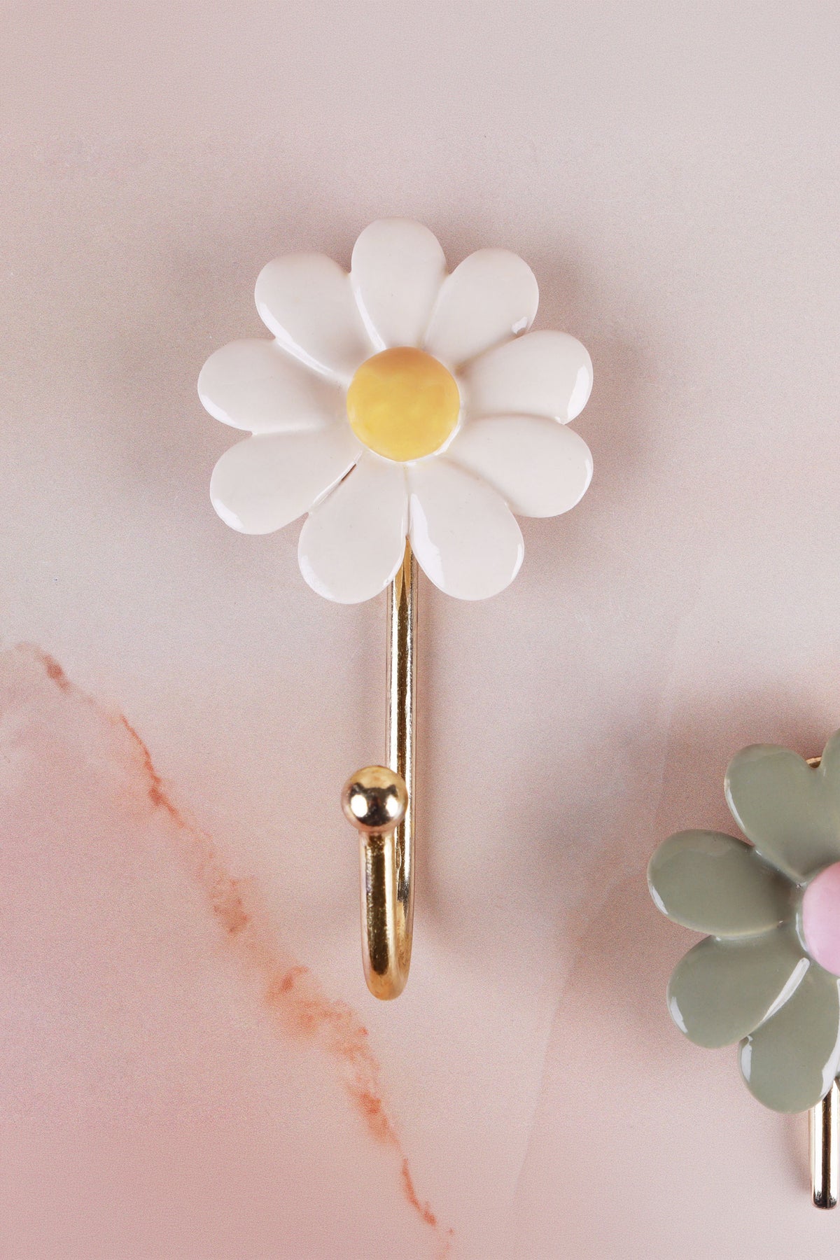 White ceramic daisy wall hook with a yellow centre on a gold-tone metal hook