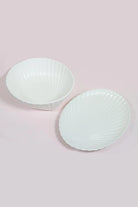 White porcelain shell bowl and oval shell dish side by side on a pale pink surface