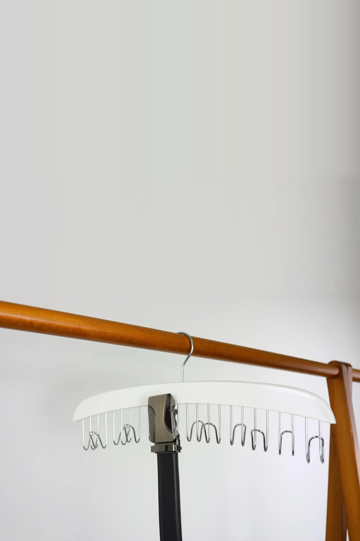 White wooden belt hanger holding a belt on a wooden rail