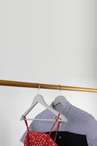 Two grey wooden coat hangers on a rail holding a striped shirt and a red dress