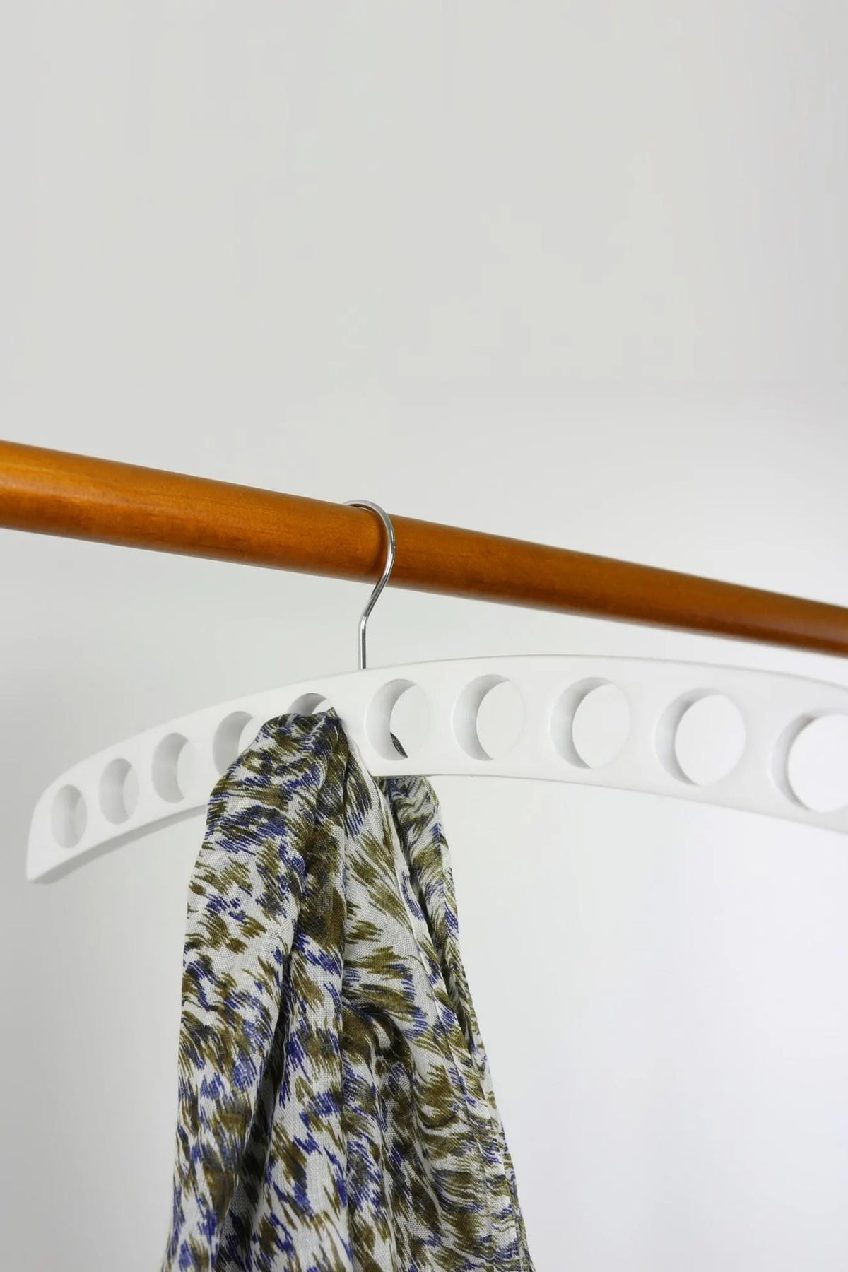 White wooden scarf hanger with round holes holding a printed scarf on a wooden rail