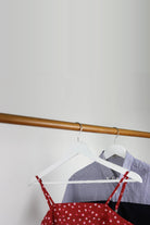 Two white wooden coat hangers on a rail holding a striped shirt and a red dress