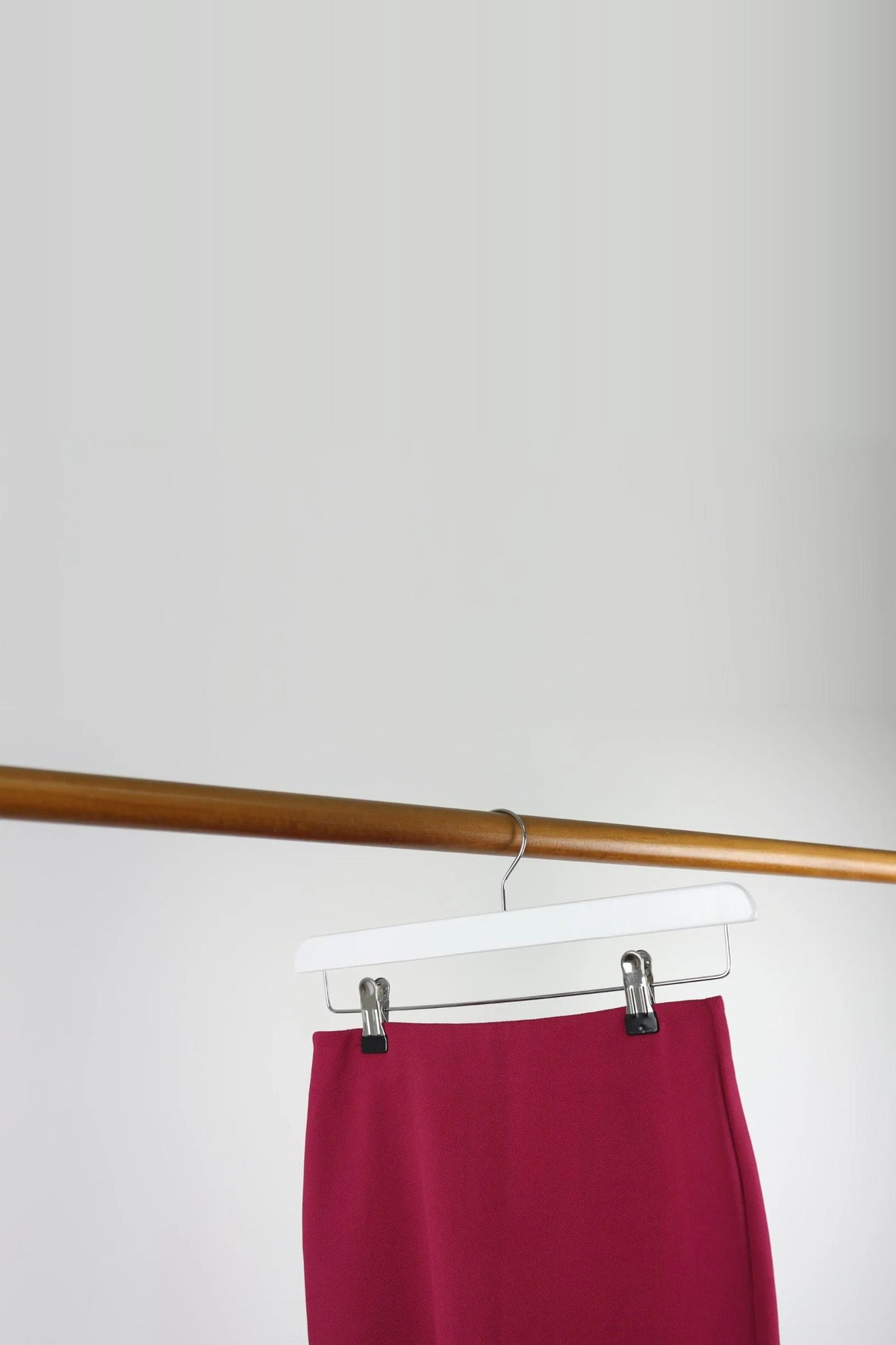 White wooden clip hanger holding a red skirt on a wooden rail
