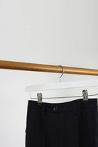 White wooden clip hanger holding black trousers on a wooden rail